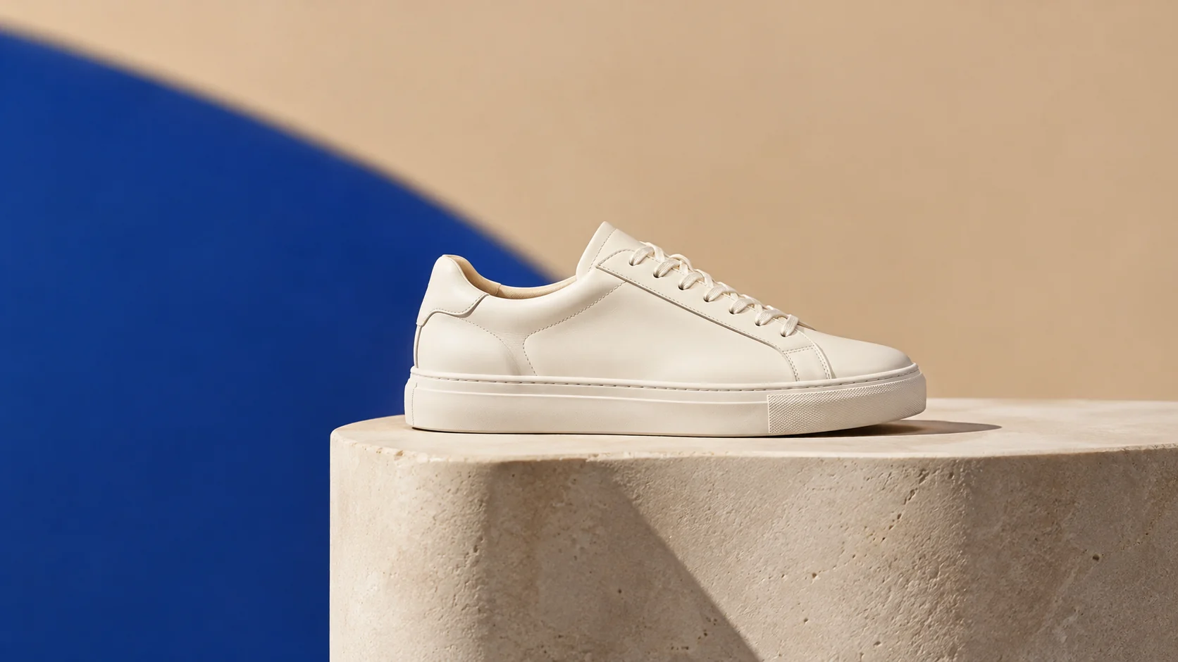 Cream leather sneaker on a pale plinth with a bold cobalt shadow